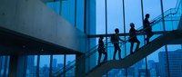 Business people silhouettes walking up modern staircase in corporate office building with glass windows and city skyline view at dusk.