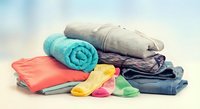 Stack of folded clothes with colorful socks on white surface. Laundry pile includes jeans, sweater, towels and bright rainbow socks for household organization.