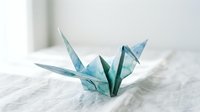 Delicate blue origami paper cranes with intricate folded wings resting on white marble surface, symbolizing peace, hope and traditional Japanese art craftsmanship.