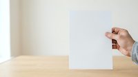 Hand holding blank white card on wooden table with neutral background, suitable for mockups, presentations, and marketing materials.