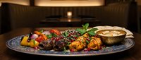 Grilled meat kebabs with colorful vegetables and sauce on decorative plate in restaurant kitchen setting for culinary and dining concepts.