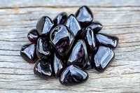 Polished black hematite gemstones arranged on rustic wooden surface for crystal healing, meditation, spiritual wellness and metaphysical practices.