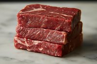 Fresh raw beef steaks stacked on marble surface with visible marbling and deep red color, showcasing premium meat quality for cooking and food service industry.