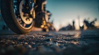 Motorcycle wheel on asphalt road at sunset with blurred background creating dramatic travel and adventure atmosphere for transportation concepts.