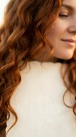 Young Caucasian woman with long curly auburn hair in warm sunlight showcasing natural texture and shine for beauty and haircare concepts.
