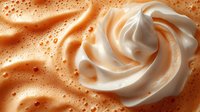 Creamy swirl of whipped cream or frosting with smooth texture against bubbly caramel background. Food styling for desserts, baking and culinary projects.