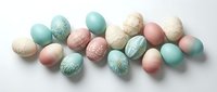 Pastel colored Easter eggs in mint green, pink and cream tones with delicate floral patterns scattered on white background for spring holiday decorations.