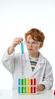 Young Caucasian boy scientist in white lab coat and safety goggles examining blue liquid in test tube with colorful chemistry set on white background.