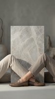 Crossed legs in beige trousers and brown leather shoes behind marble stone slab in modern minimalist interior setting for contemporary design projects.