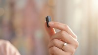 Close-up of female hand holding small black USB flash drive with wedding ring, soft bokeh background for technology and data storage concepts.