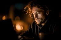 Middle-aged Caucasian man with curly hair in contemplative mood, warm candlelight creating atmospheric bokeh background for storytelling projects.