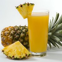 Fresh pineapple juice in tall glass with ripe cut pineapple slices and whole fruit on white background, tropical refreshing drink for summer menu.