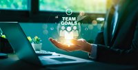 Business professional holding glowing team goals icons with people symbols above open palm in modern office workspace for corporate strategy planning.
