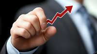 Businessman in dark suit pointing at upward trending red arrow graph showing growth and success, representing positive business performance and progress.