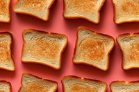 Crispy golden toast slices arranged in rows on vibrant coral background, creating minimalist food pattern for breakfast concept.