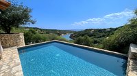 Luxurious infinity pool with crystal blue water overlooking scenic lake and rolling hills, stone walls frame modern swimming pool against natural landscape backdrop.