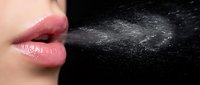 Woman's lips releasing fine water droplets spray mist against dark background for health hygiene and respiratory concepts.