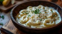 Creamy tortellini pasta in rich white sauce garnished with fresh herbs and black pepper, served in rustic wooden bowl on dark background. Perfect for food menu.