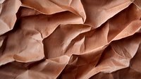 Crumpled dusty rose colored paper creating abstract textural waves and shadows. Artistic background with organic folds and creases for modern design projects.