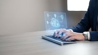 Professional businessman using laptop with holographic digital interface displaying global network connections and data analytics in modern office environment.