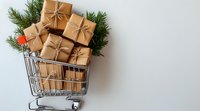 Shopping cart filled with kraft paper wrapped Christmas presents and pine branches on light background, holiday shopping concept with copy space.