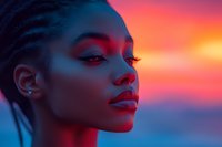 Young African American woman with glowing skin in dramatic neon lighting against vibrant sunset background, showcasing creative beauty makeup and profile pose.
