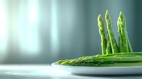 Fresh green asparagus spears arranged on white plate against blurred teal background. Minimalist food photography highlighting natural organic produce.