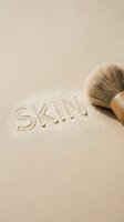 Makeup brush with natural bristles creating the word "SKIN" on beige powder surface, representing cosmetics, beauty application, skincare routine, and professional makeup artistry techniques.