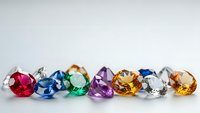 Colorful faceted gemstones collection featuring ruby, sapphire, emerald, amethyst, topaz and diamond crystals arranged on white background for jewelry design.