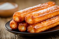 Fresh homemade churros coated in cinnamon sugar served on dark plate against rustic wooden background, traditional Spanish dessert pastry for cafe menu.
