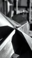 Close-up of folded metal sheets with sharp creases and reflective surfaces in monochrome, suitable for industrial, manufacturing, and design projects.