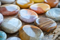 Polished semiprecious gemstones in soft pastel colors arranged on wooden surface, showing natural patterns and textures in agate and crystal specimens.