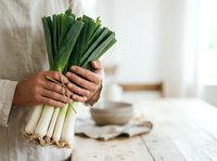 Fresh green leeks held in hands against neutral kitchen background, ready for cooking and meal preparation.