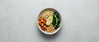 Healthy vegan Buddha bowl with quinoa, chickpeas, roasted sweet potato, kale, and avocado on a light gray background, top view.