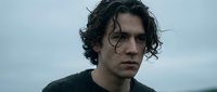 Young man with dark curly hair and intense expression against moody sky background for dramatic storytelling and character development projects.