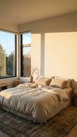 Serene bedroom interior with unmade bed, neutral bedding, large windows with natural light, minimalist decor, and warm earth tones for home design.