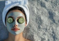 Young Asian woman relaxing with green clay facial mask and cucumber slices on eyes at spa. Wellness and skincare concept for beauty treatment.