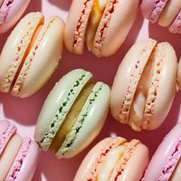 Colorful French macarons in pastel pink, peach, mint green and cream shades arranged on pink background, sweet meringue cookies with filling pattern.