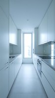 Modern white galley kitchen with stainless steel countertops, sleek cabinetry, and natural light from window. Ideal for interior design, home renovation, and real estate marketing.