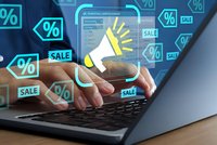 Digital marketing concept with hands typing on laptop surrounded by floating sale percentage icons and megaphone symbol for online advertising campaigns.