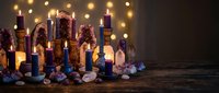 Mystical altar with colorful candles, crystals and gemstones on wooden surface with warm bokeh lights creating magical spiritual atmosphere for meditation rituals.