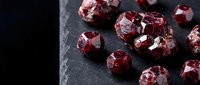 Raw red garnet gemstones with natural crystalline facets scattered on dark slate surface for jewelry making and mineral collection displays.