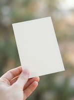 Hand holding blank white paper card against blurred natural background for mockup design templates and promotional materials.