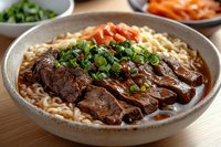 Tender braised beef slices served on Asian noodles in savory brown sauce, garnished with fresh green onions and chili in ceramic bowl on wooden surface.