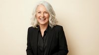 Happy mature Caucasian businesswoman with silver gray hair laughing in black blazer against beige background for corporate headshots and professional portraits.