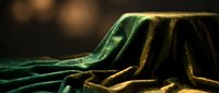 Luxurious emerald green velvet fabric with golden highlights draped elegantly, creating rich folds and texture for premium design projects.