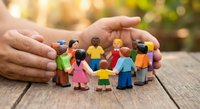 Hands protecting diverse group of miniature people figures in circle on wooden surface symbolizing community care, teamwork and social unity concept.