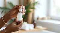 Hands holding white cosmetic bottle with pump dispenser in bright bathroom setting with plants and natural light for skincare product promotion.