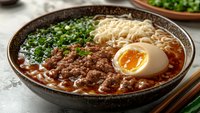 Spicy ramen bowl with tender minced meat, soft-boiled egg, fresh chopped green onions and noodles in rich aromatic broth served in ceramic bowl.