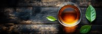 Cup of aromatic tea with fresh green leaves on dark wooden background, top view panoramic shot with warm glowing light and rustic texture.